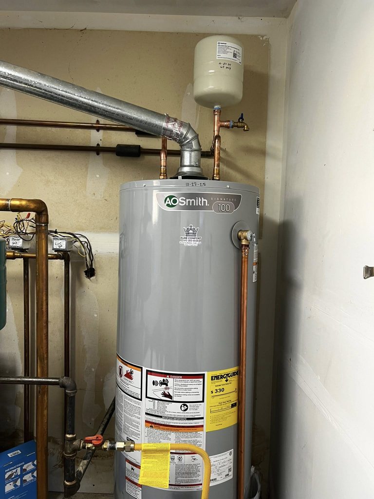 A gray A.O. Smith water heater with pipes attached sits in a utility room. Labels and warnings are visible on the tank. The environment is industrial.